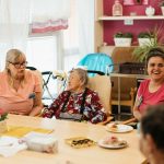 Elderly residents and caregivers enjoying a meal and conversation in a cheerful dining space.